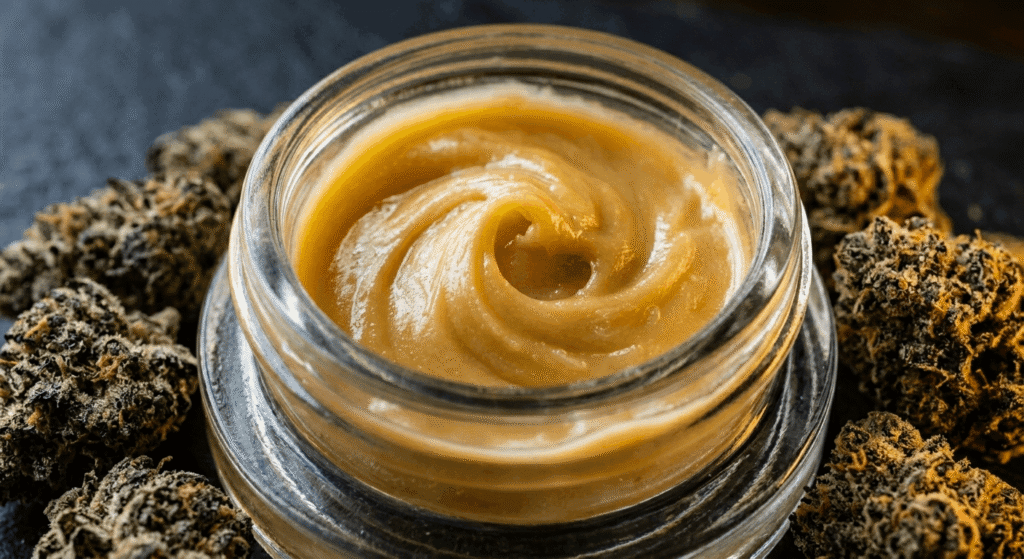 Close-up of golden THCa badder concentrate in glass jar surrounded by terpene-rich hemp flower buds
